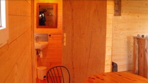 A wooden interior with a small bathroom, a chair, and a table. - Cabane des cerfs (Allons)