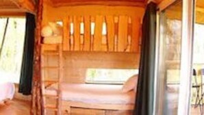 A wooden cabin interior with a bed, a chair, and a table. - Cabane des cerfs (Allons)