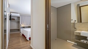 A hotel room with a walk-in closet, a bed, a shower area, and a bathroom with a sink and mirror. - Slim Guarapuava (Guarapuava)