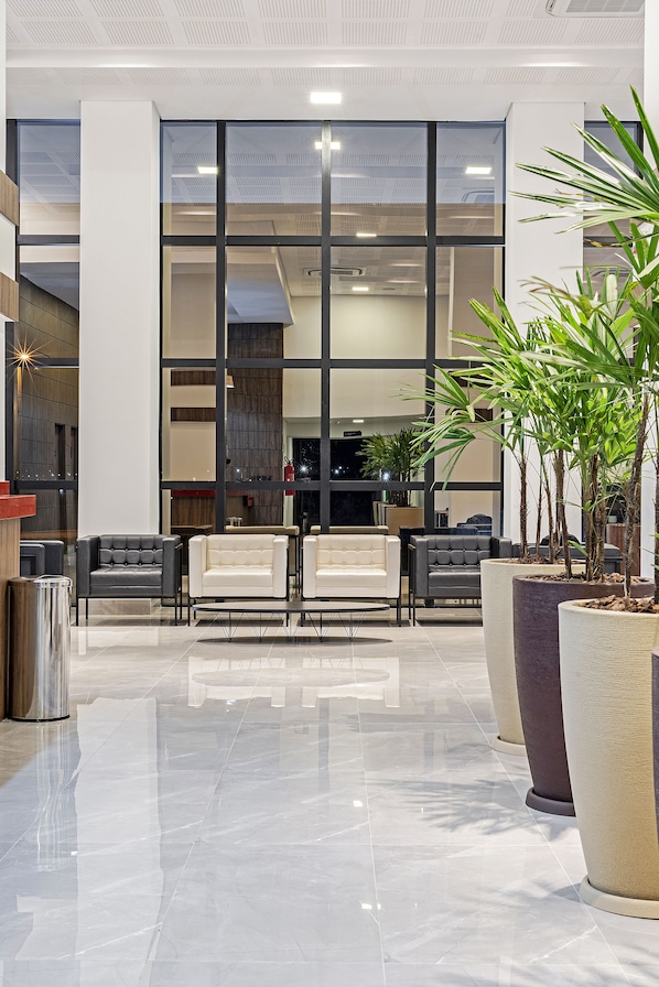 A modern lobby with a glass wall, seating area, and potted plants.
