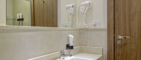 Une salle de bain moderne avec un grand miroir, deux lavabos et un sèche-cheveux fixé au mur.