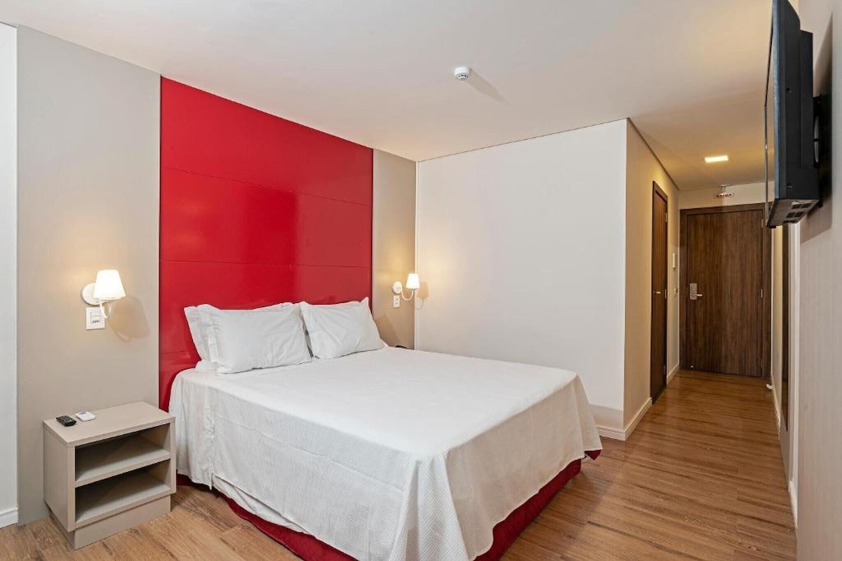 A hotel room with a bed, bedside tables, and a TV mounted on the wall.