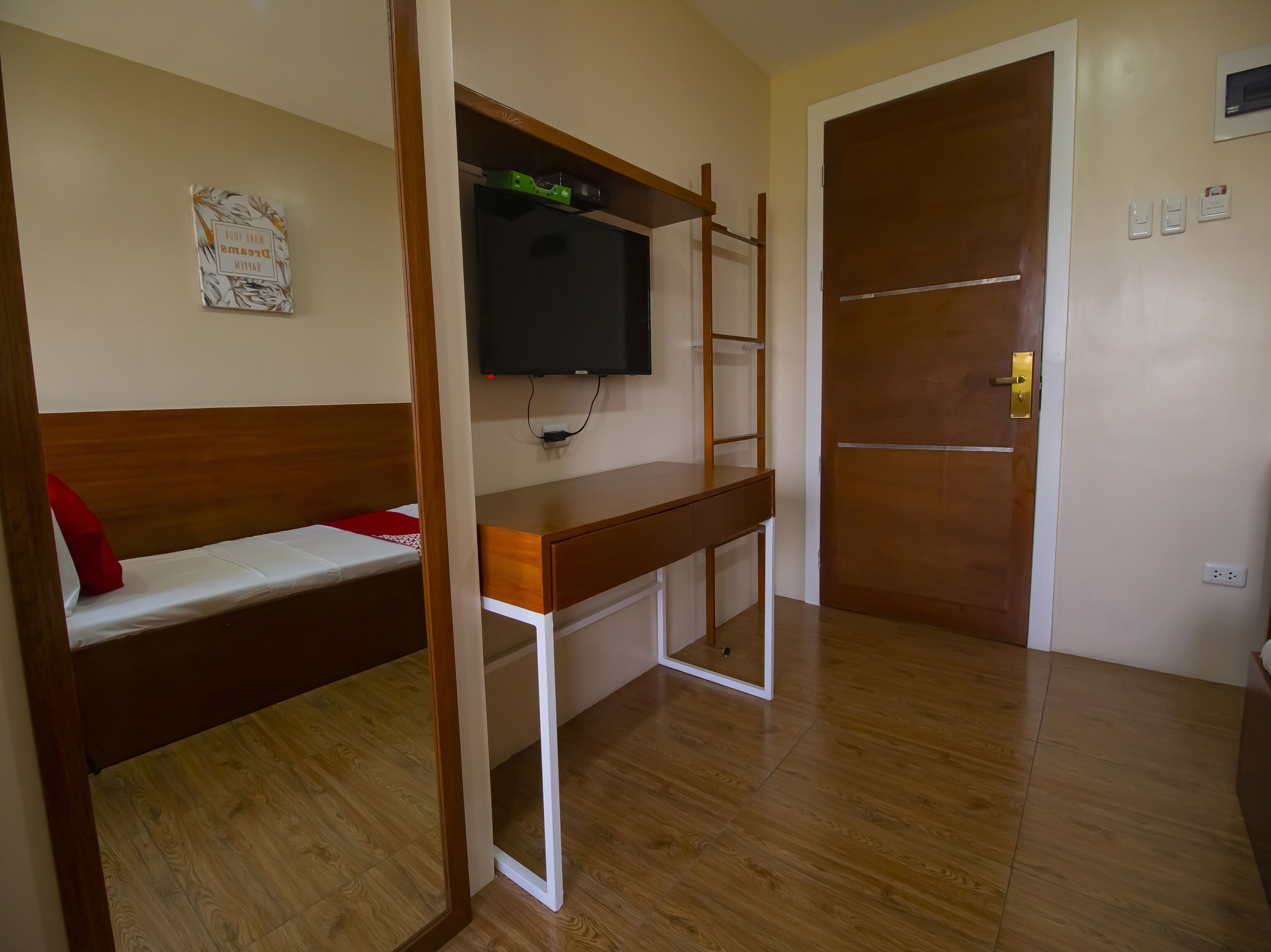 A room with a bed, a desk with a TV, and a door.