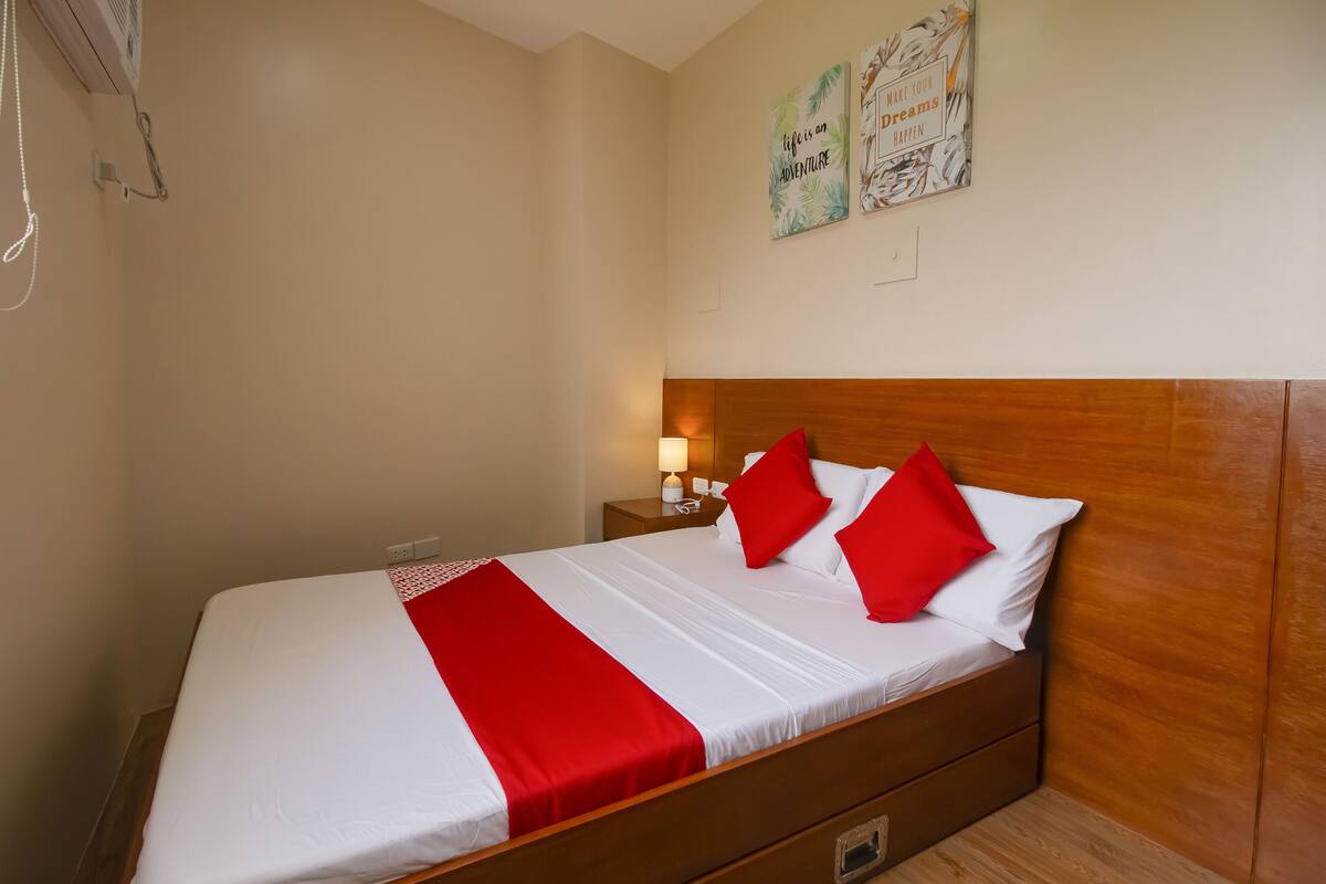 A neatly made bed with red and white bedding, a wooden headboard, and a nightstand with a lamp.
