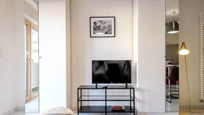 Una sala moderna con una televisión de pantalla plana sobre un mueble negro, un cuadro en la pared y una lámpara de pie.