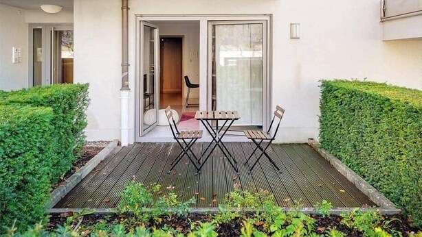 Un patio exterior moderno con una mesa y sillas de madera, rodeado de setos bien cuidados.
