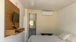 Un dormitorio con cama, televisor montado en un panel de madera, mesita de noche y unidad de aire acondicionado en la pared.