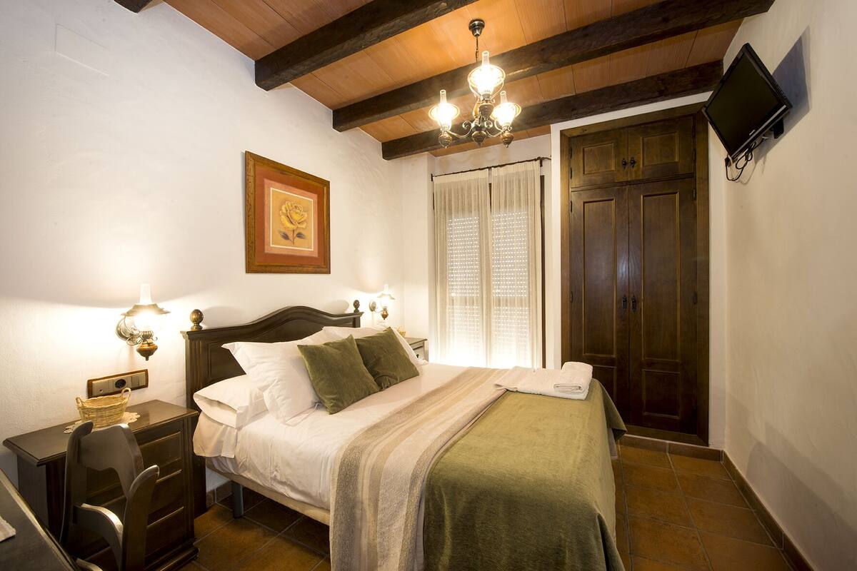Quarto com cama, luminárias de cabeceira, televisão, porta de madeira e quadro pendurado na parede.