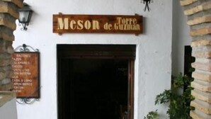 En rustik entré med en skylt som visar texten ”Meson de Guzman” och en valvformad öppning av tegelstenar.
