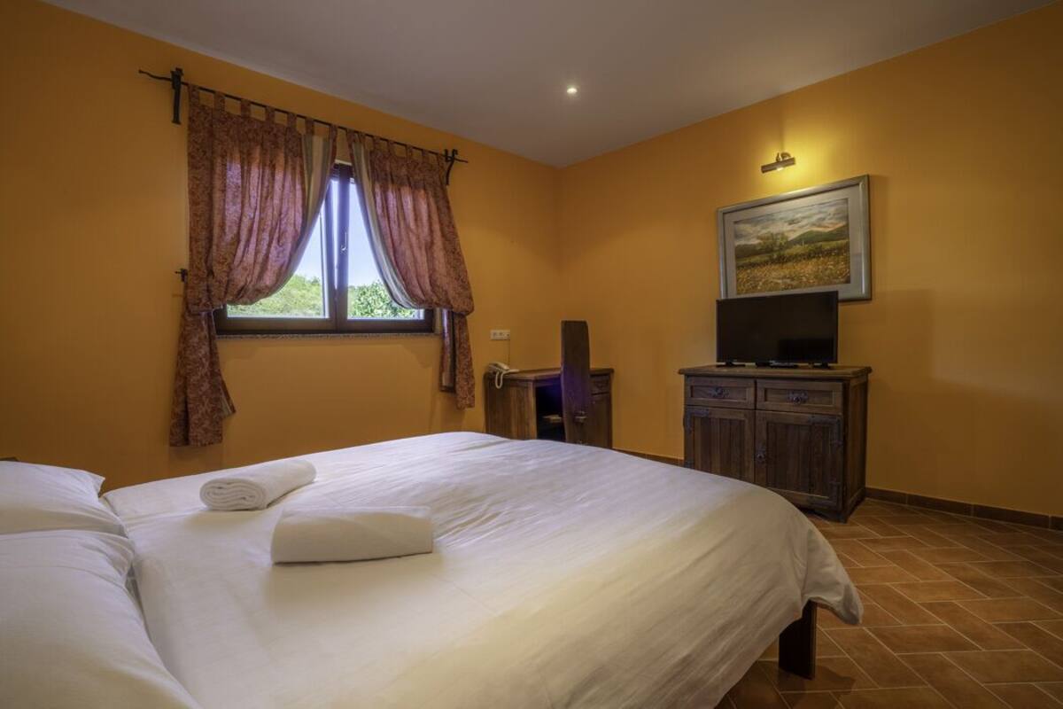 Ein Hotelzimmer mit einem Bett, einem Fernseher, einem Schreibtisch und einem Fenster mit Vorhängen.