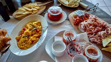 Un desayuno con huevos revueltos, queso y embutidos sobre una mesa de madera.