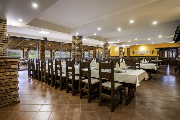 Un restaurant doté de longues tables et de chaises en bois, de piliers en briques et de grandes fenêtres donnant sur l’extérieur.