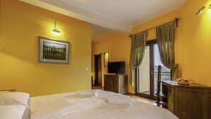 A hotel room with a large bed, a television, a wooden dresser, and a balcony with curtains.