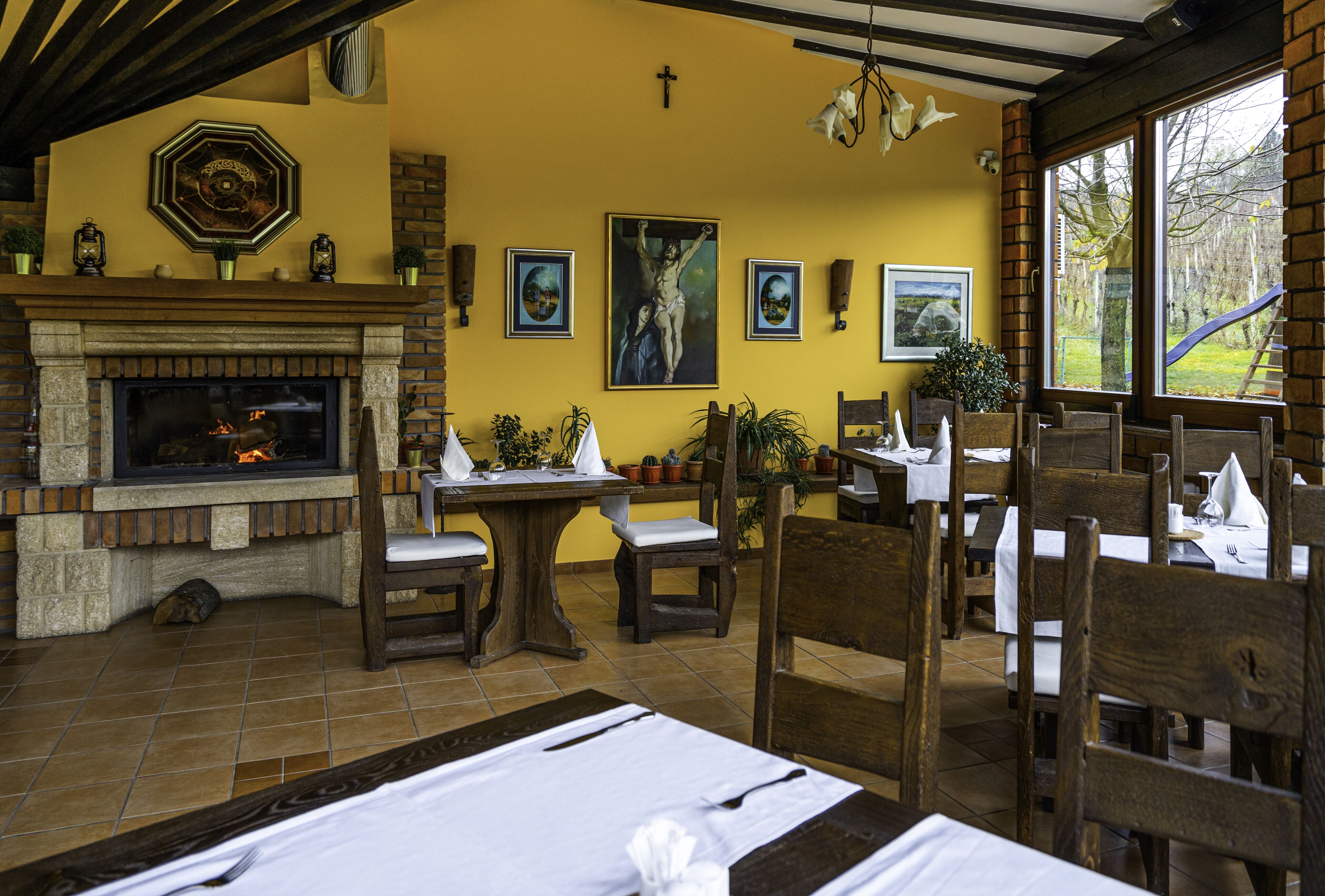 A dining area with wooden tables and chairs, a fireplace, and various framed artworks on the walls.