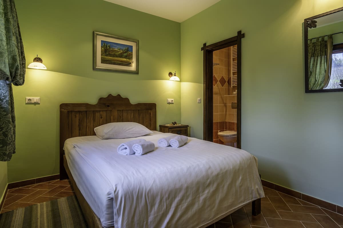 Ein Schlafzimmer mit einem Bett, einem Nachttisch, einer Wandlampe, einem gerahmten Bild und einer Dusche.