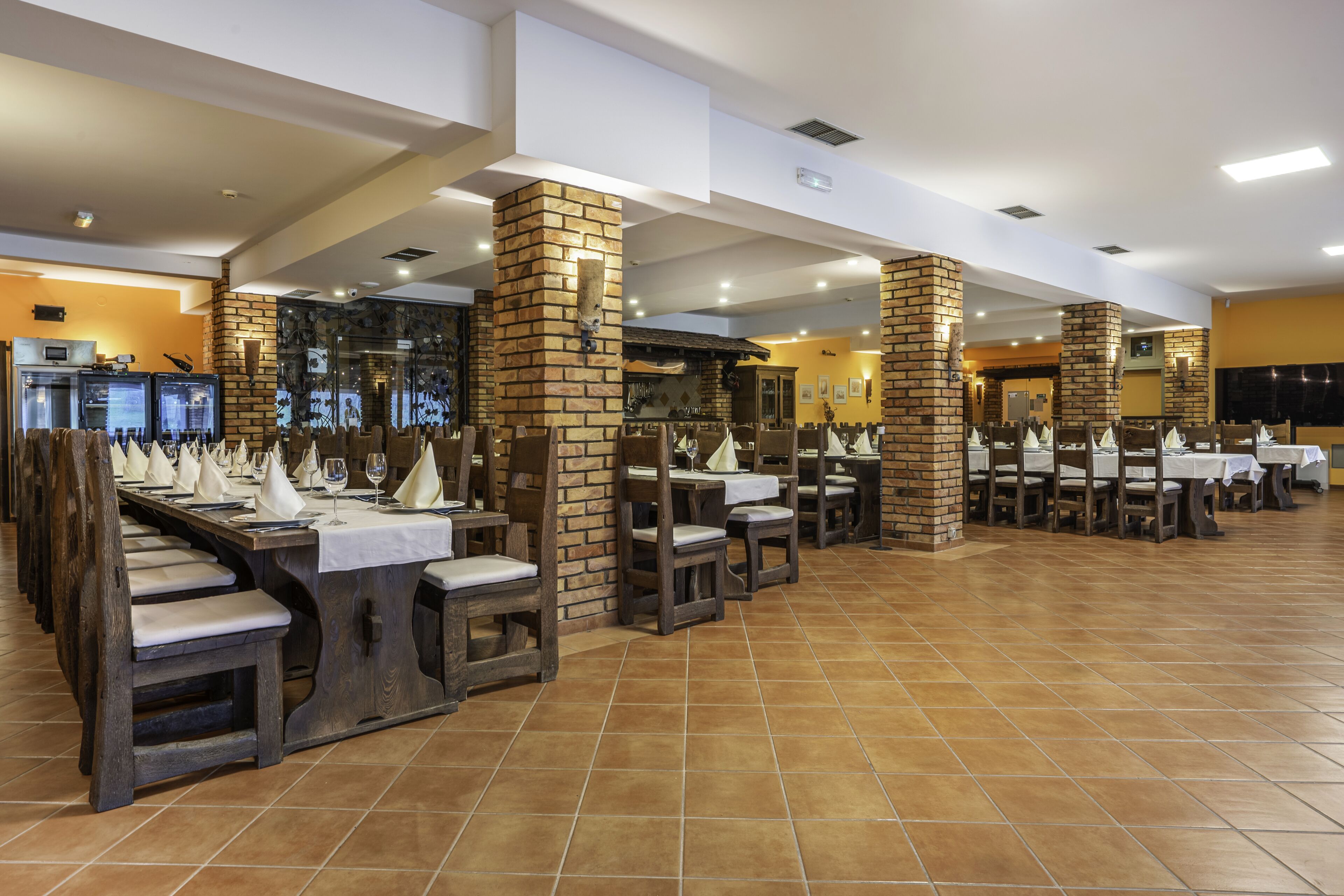 A restaurant with multiple tables and chairs, brick pillars, and a tiled floor.