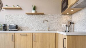 Una cocina moderna con armarios de madera, encimera blanca, tostadora, lavabo y salpicadero con azulejos pequeños.
