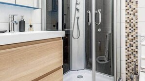 Un baño moderno con cabina de ducha de vidrio, tocador de madera y salpicadero de azulejos.