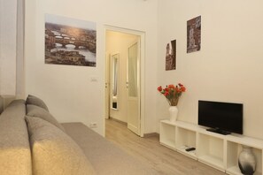 Una sala de estar con un sofá, un televisor, un jarrón con flores y un cuadro en la pared.