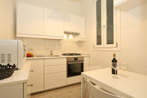 Una cocina moderna con armarios blancos, horno empotrado, microondas y comedor con mesa y sillas.