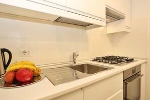 Una cocina con un lavamanos de acero inoxidable, una estufa a gas y un frutero con plátanos y manzanas.