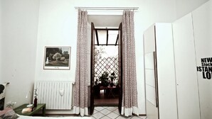 A room with a bed, a bedside table with a lamp, a framed picture on the wall, and a view through a doorway to a dining area.