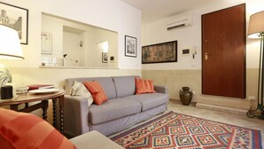 Una sala de estar con un sofá gris, un tapete estampado y una puerta de madera.