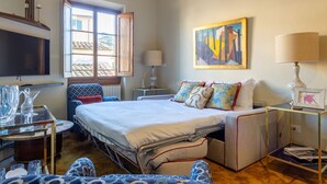 Una habitación de hotel con una cama, una silla, una mesa, una lámpara y un cuadro en la pared.