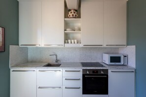 Cocina compacta con armarios blancos, microondas, fregadero y lavavajillas.