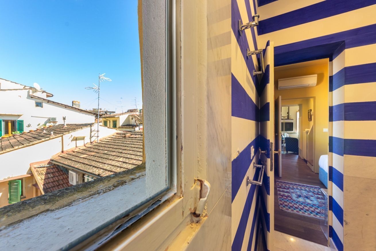 A hotel room with a window overlooking a residential area, a hallway with striped walls, and a visible air conditioning unit.