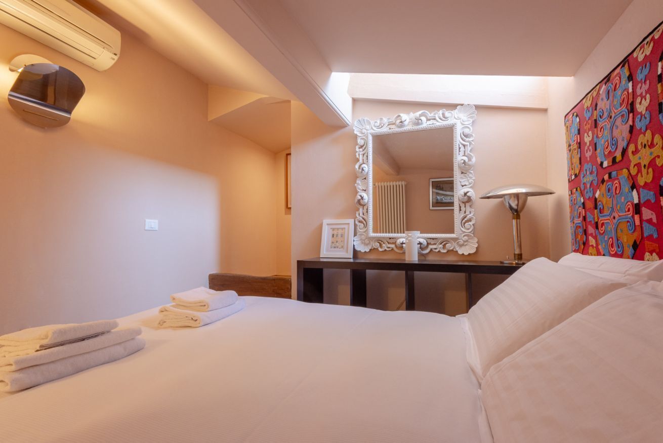 Habitación de hotel con cama, un espejo grande, un escritorio con lámpara y una obra de arte colorida en la pared.