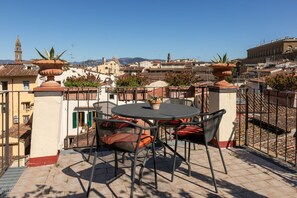 Una terraza con una mesa redonda y sillas, con vistas a un paisaje urbano con edificios y una torre.