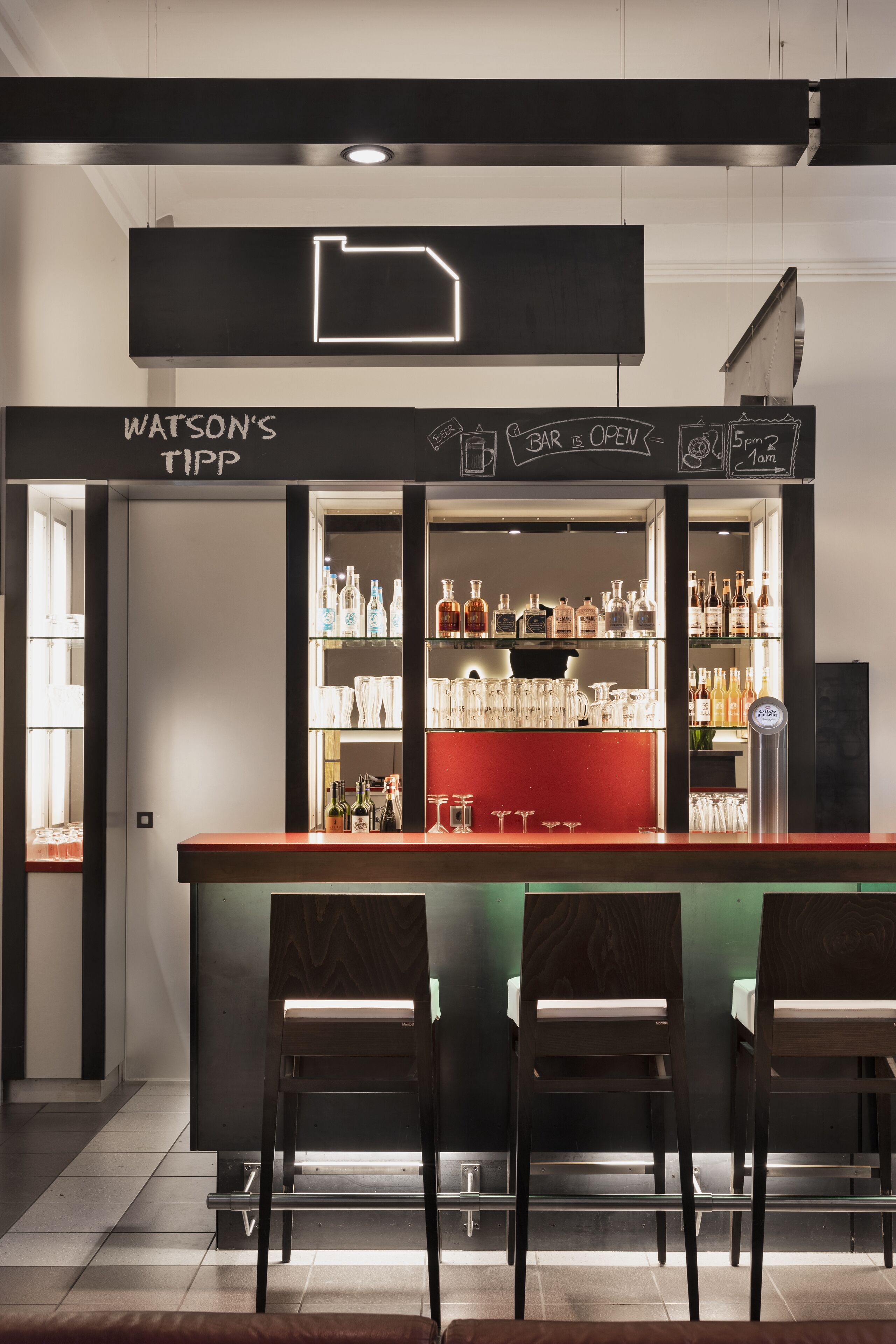 A bar area with a neon sign, shelves of bottles, and two bar stools.