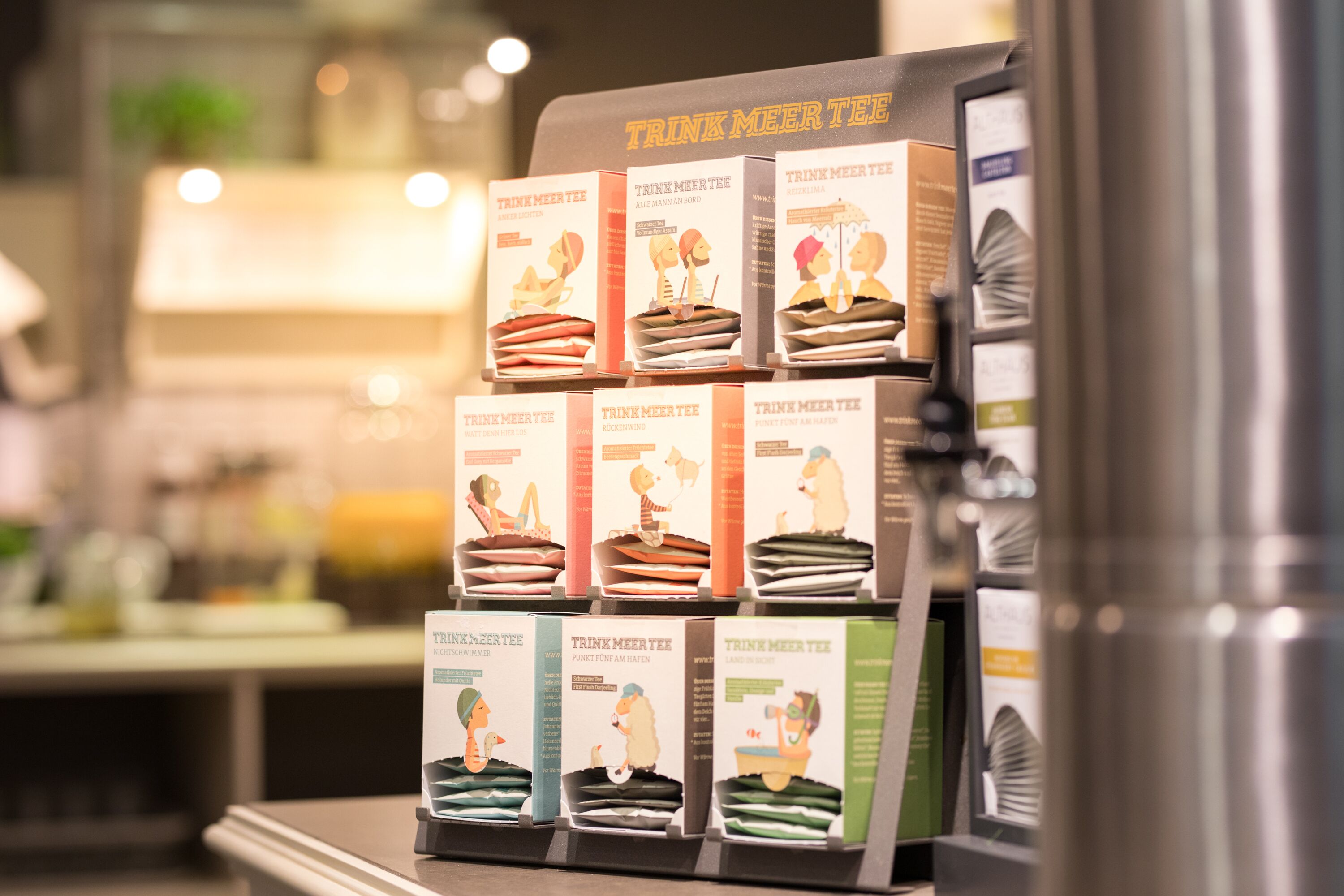Une étagère dans un magasin présente une collection de boîtes de thé de la marque « Trink Meer Tee ».