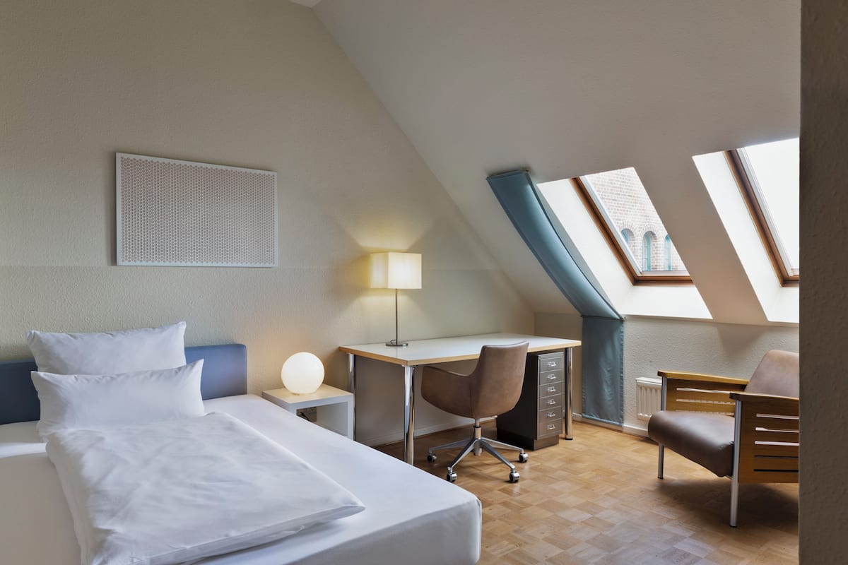 Ein Hotelzimmer mit Bett, Schreibtisch, Stuhl und Dachfenster.