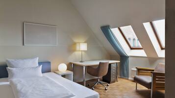 Habitación de hotel con cama, escritorio, silla y tragaluz.