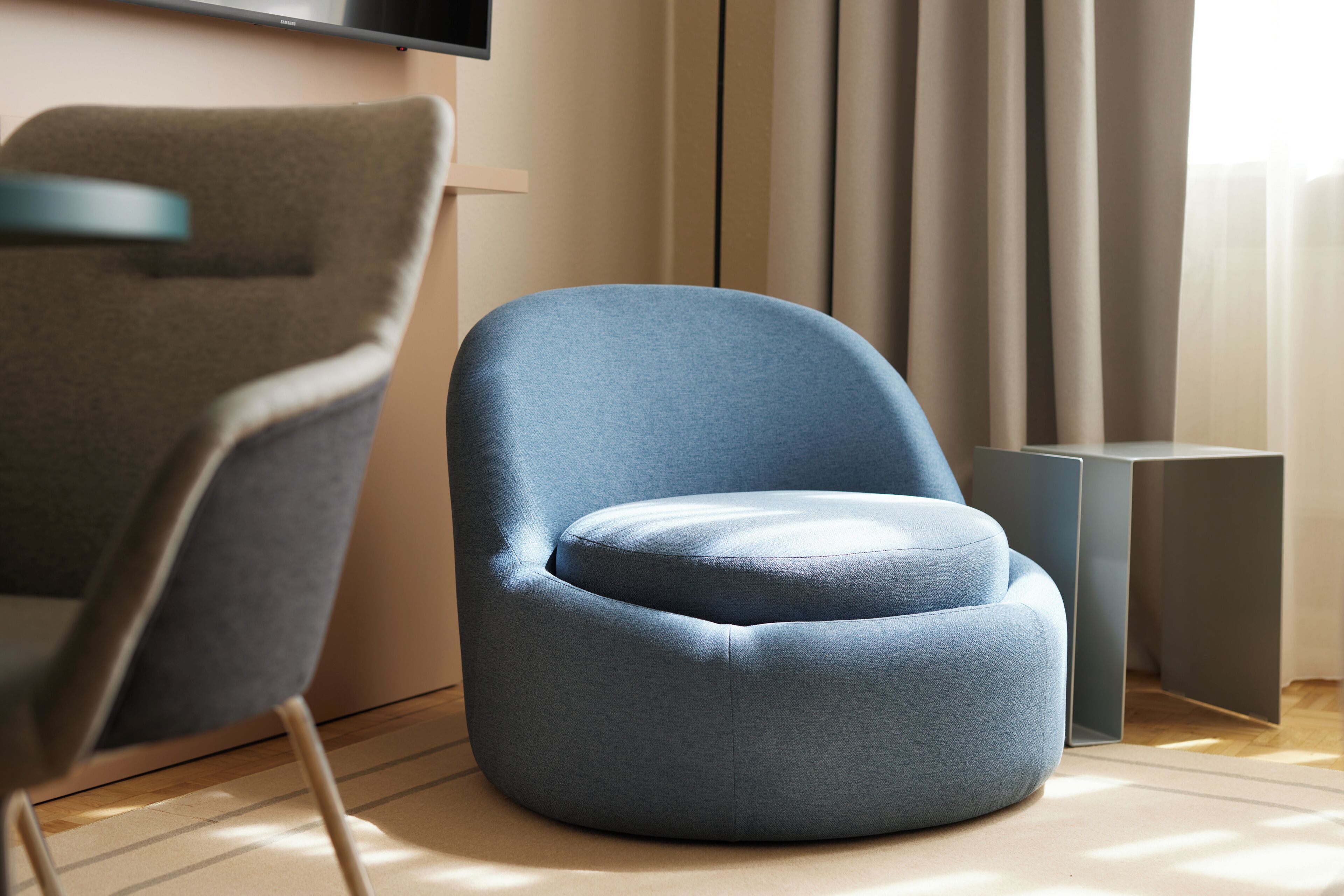 Ein modernes Zimmer mit blauem Ohrensessel, grauem Sessel und minimalistischem Beistelltisch.