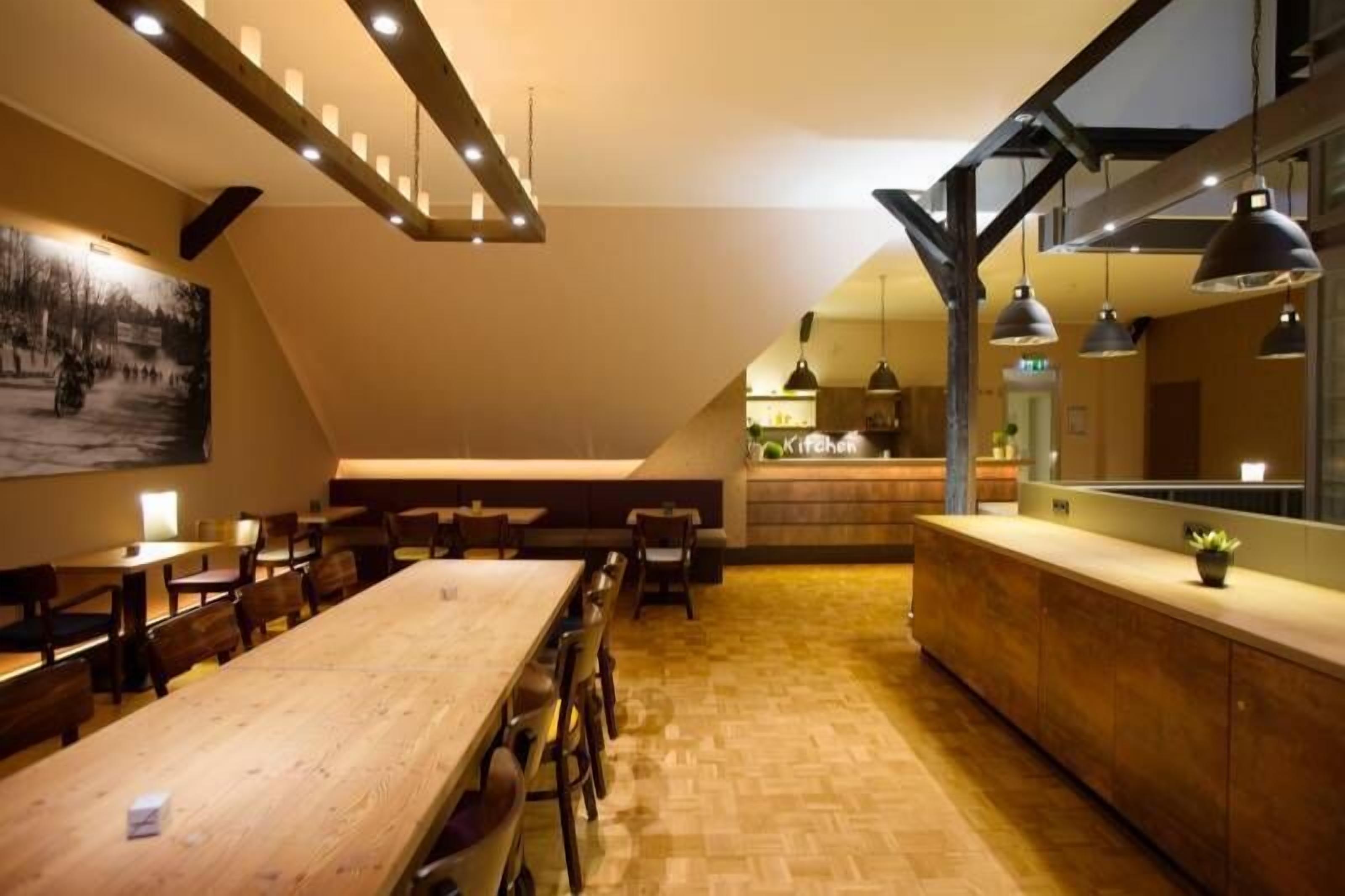 A modern interior with a long wooden dining table, benches, and a kitchen area with hanging pendant lights.