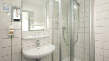 Un baño moderno con ducha de vidrio, lavabo blanco y secador de manos.