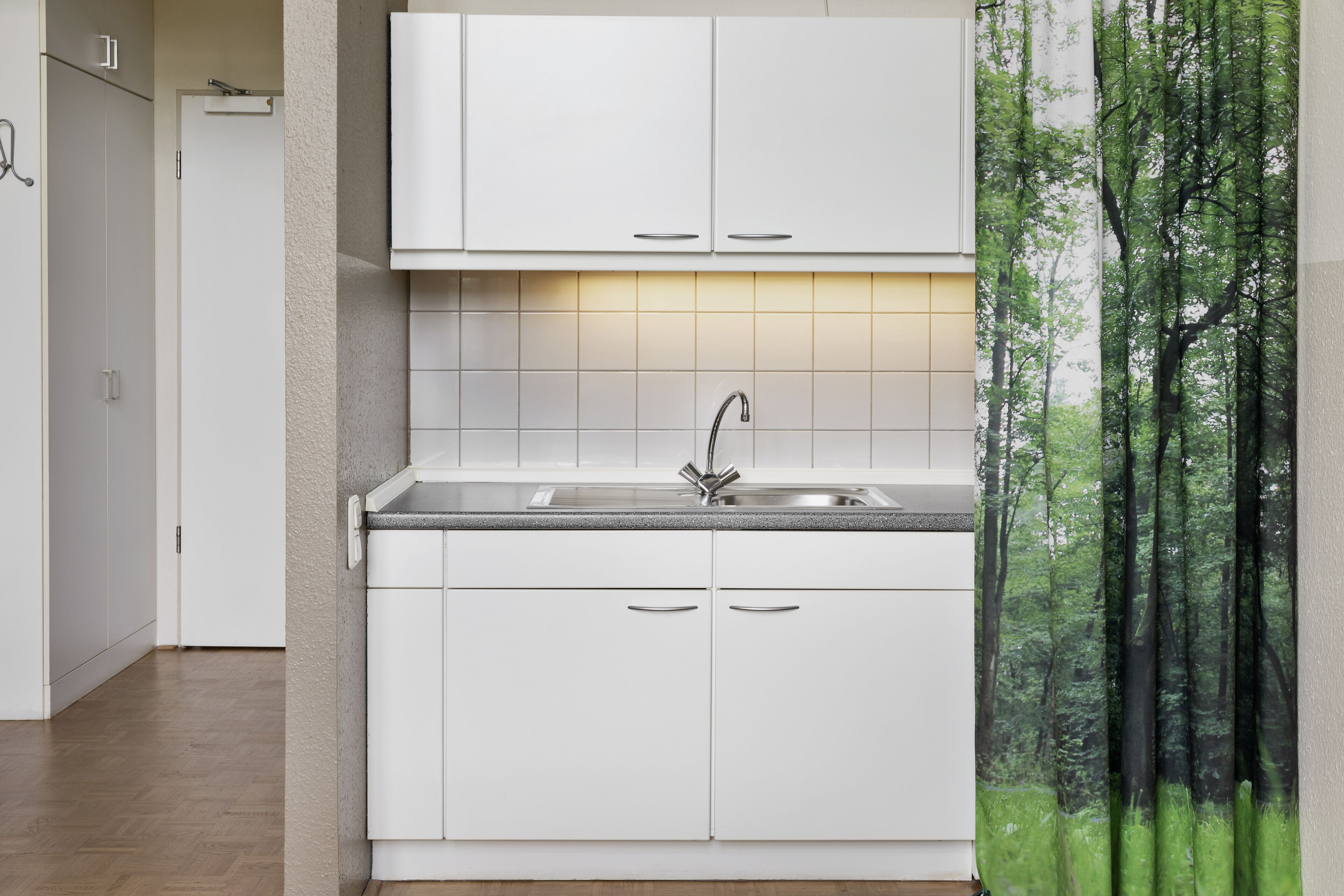 A modern kitchen with white cabinets, a stainless steel sink, and a tiled backsplash.