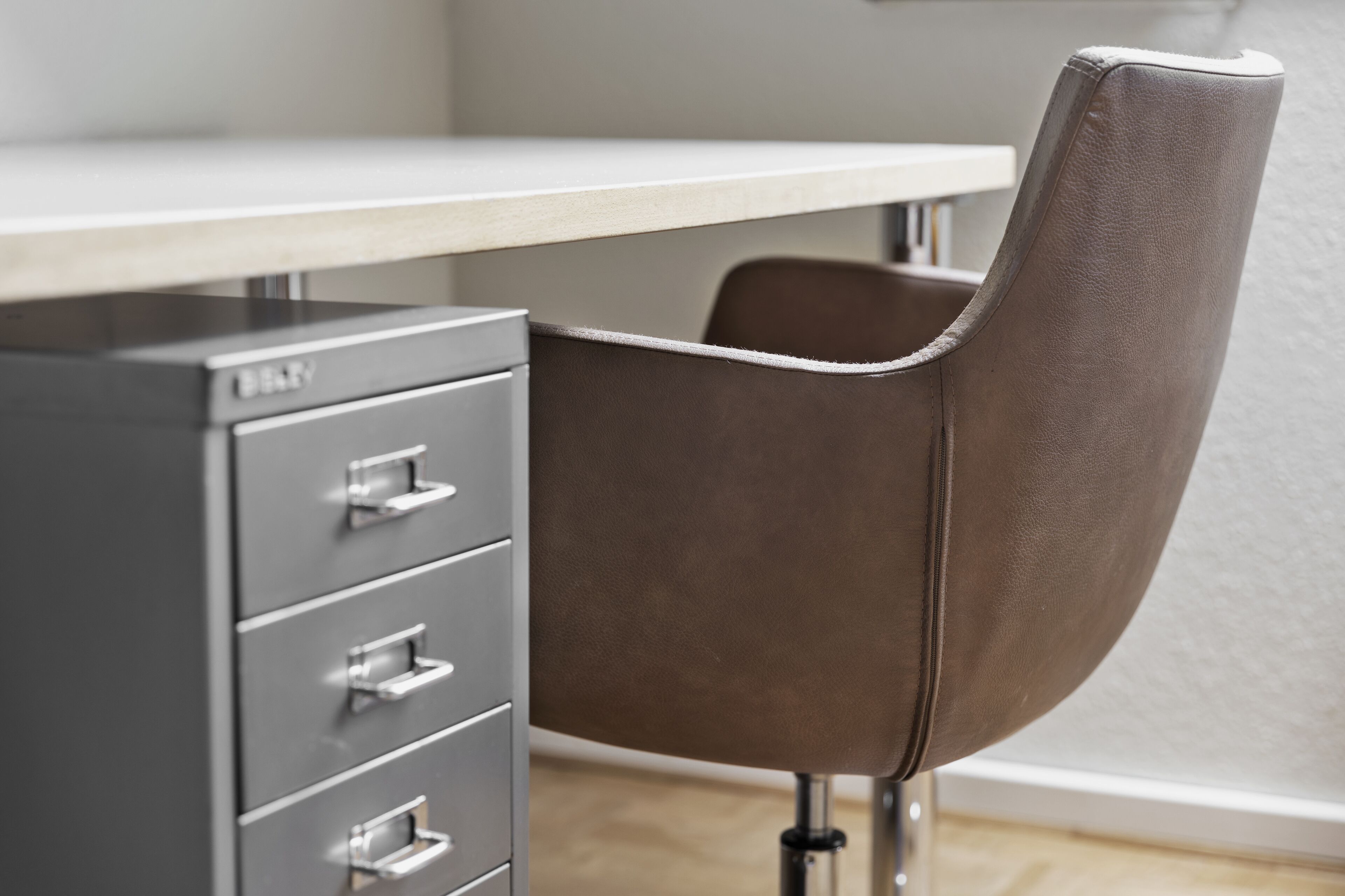 A modern office chair with a leather seat and backrest, positioned next to a metal filing cabinet with drawers.