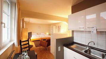 Een compacte hotelkamer met een kitchenette, een bed, een klein zithoekje en een raam met gordijnen.