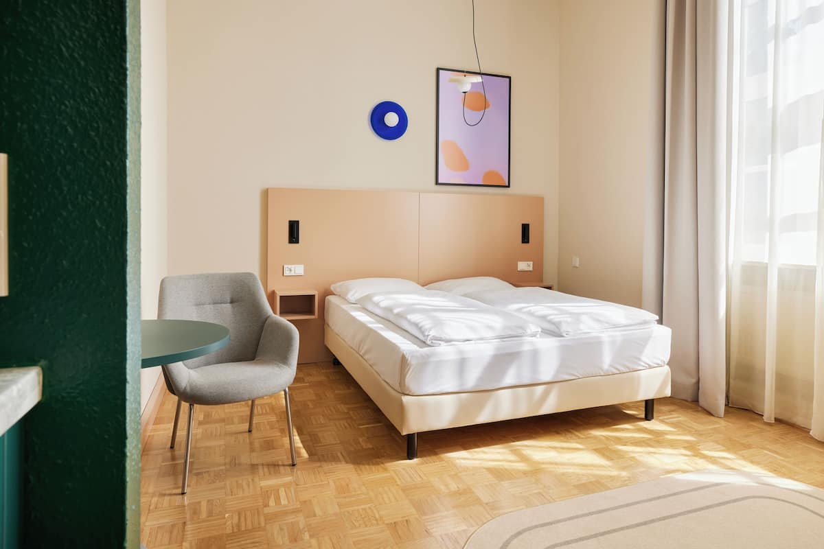Ein modernes Schlafzimmer mit einem Bett, einem Sessel, einem kleinen Tisch und einem Wandbild.