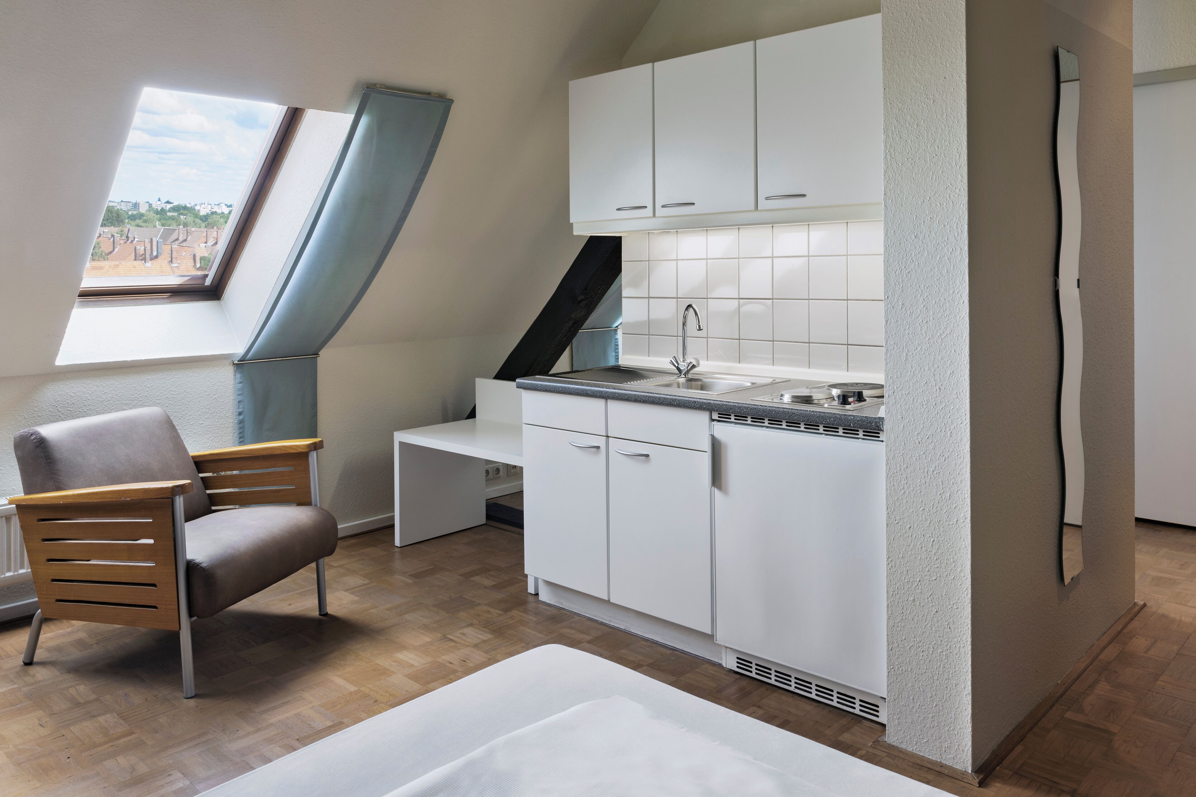 Een compact keukenhoekje met witte kastjes, een spoelbak en een raam met uitzicht op gebouwen.