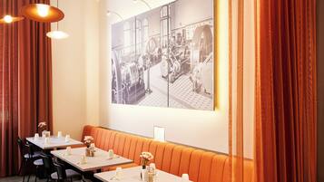 A dining area with tables set for service, a long orange booth, and a large black-and-white industrial photo on the wall.