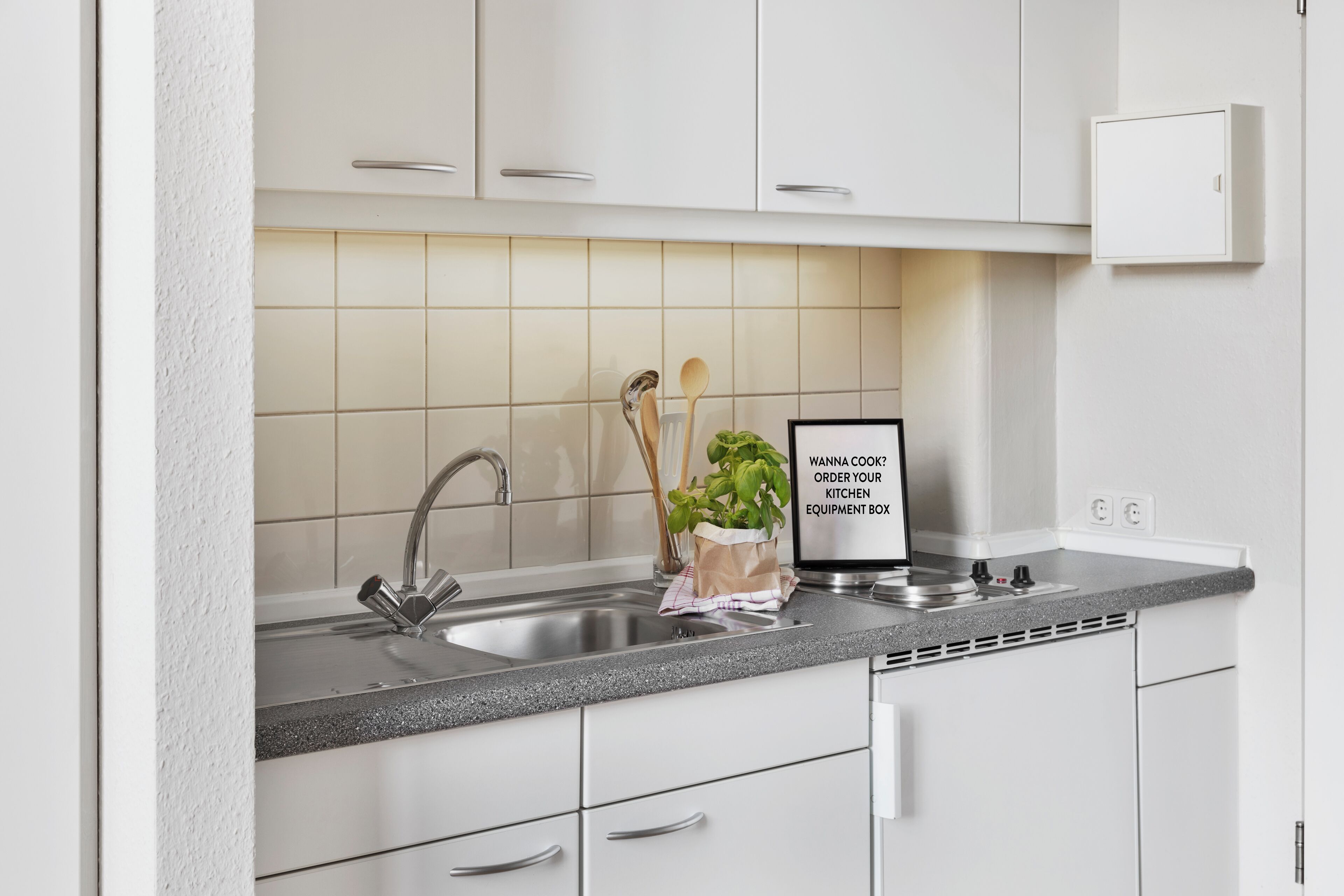 A kitchen with a stainless steel sink, a countertop, and a cabinet with a sign.