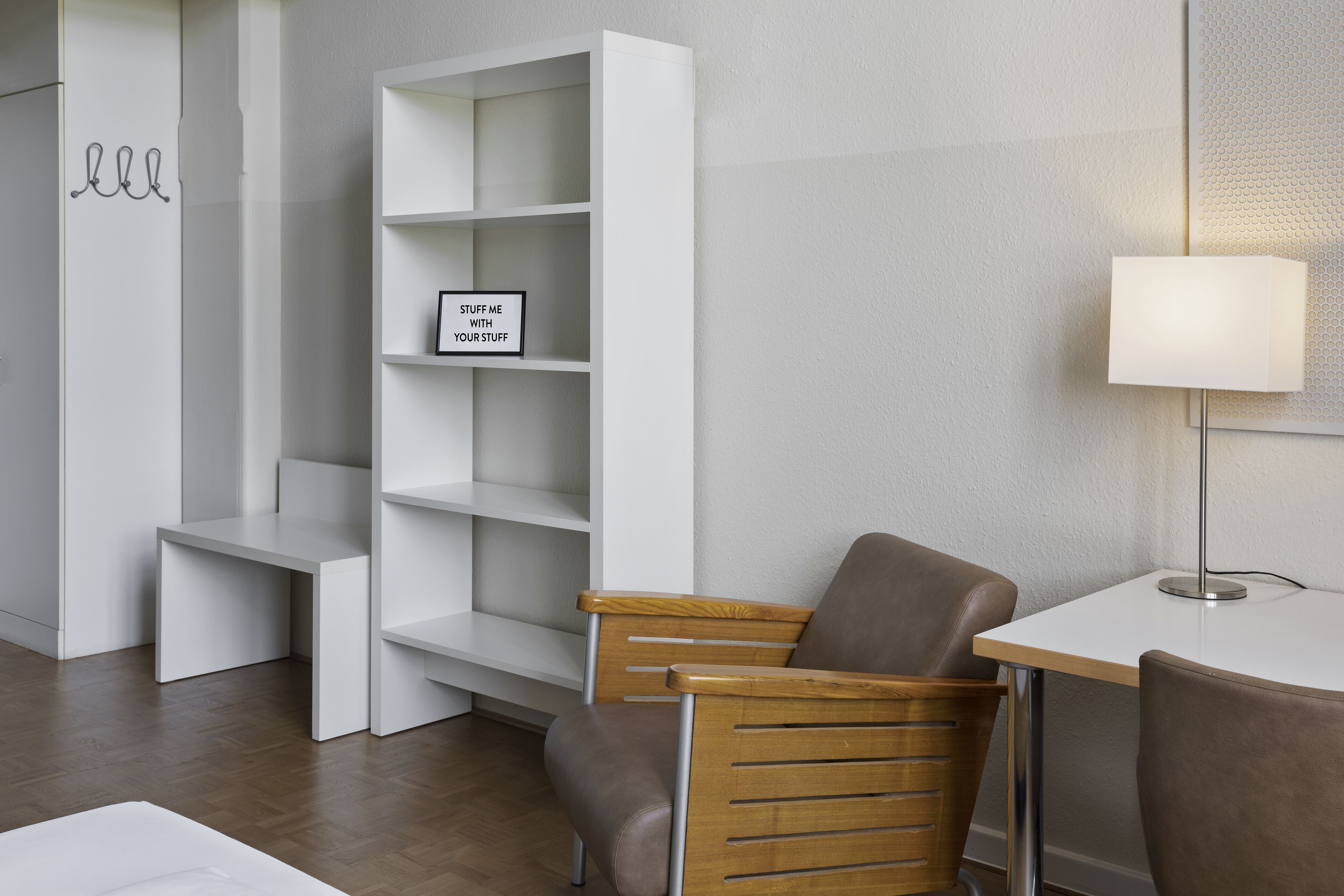 A modern room with a white bookshelf, a small table with a lamp, and two chairs.