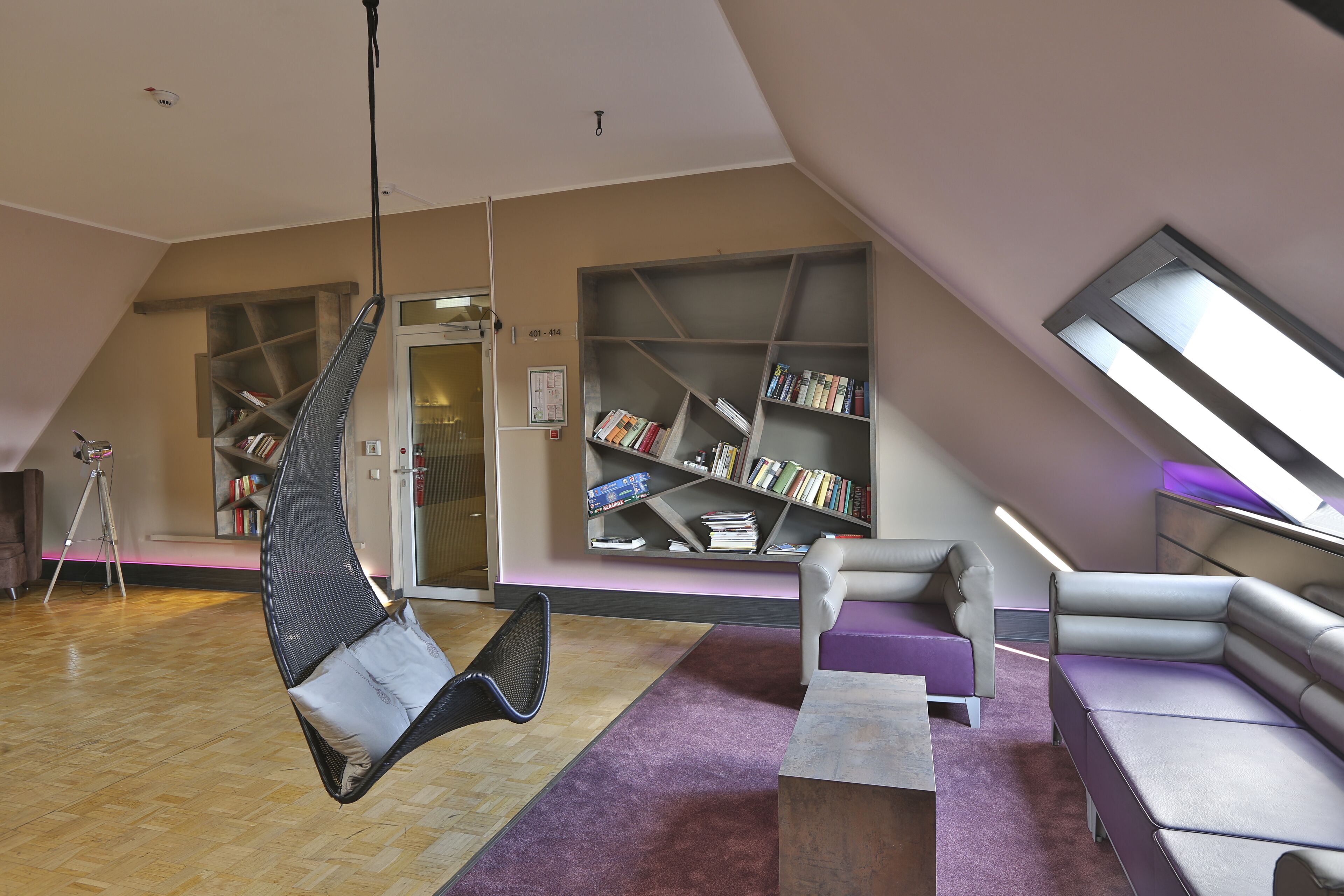 Een moderne bibliotheek met een hangstoel, boekenkasten en een schuine plafond.