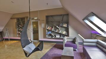 A modern library with a hanging chair, bookshelves, and a sloped ceiling.
