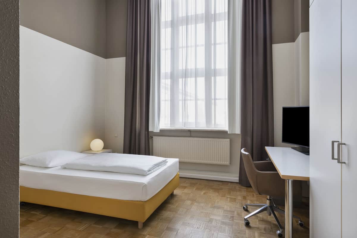 Ein modernes Hotelzimmer mit Bett, Schreibtisch, Stuhl und einem großen Fenster mit Vorhängen.